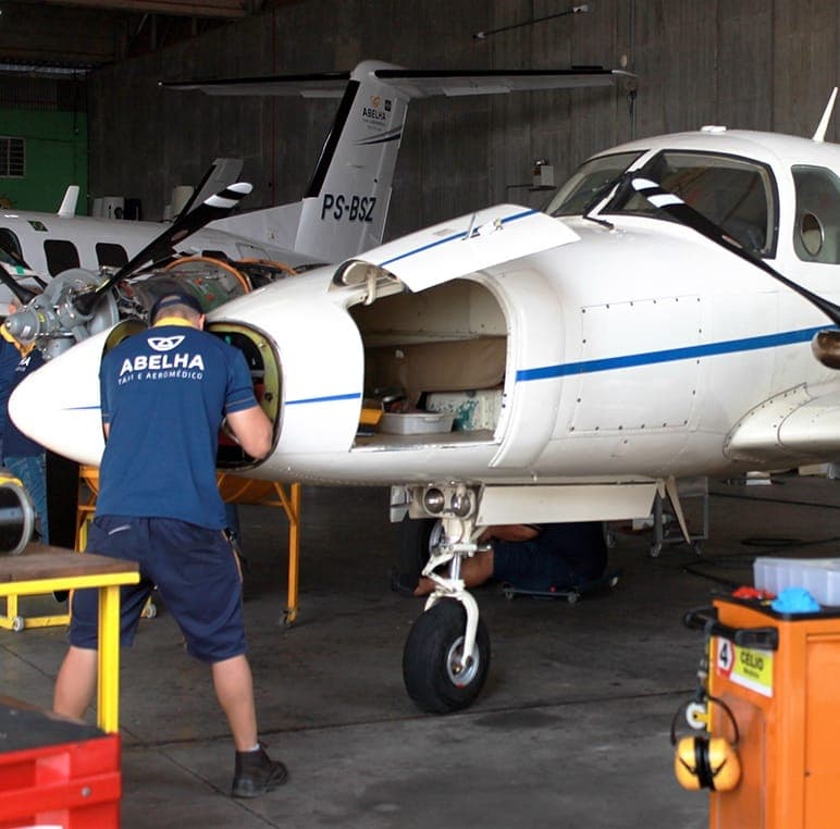 Mecânicos da Abelha trabalhando no motor de um Cheyenne dentro do hangar.